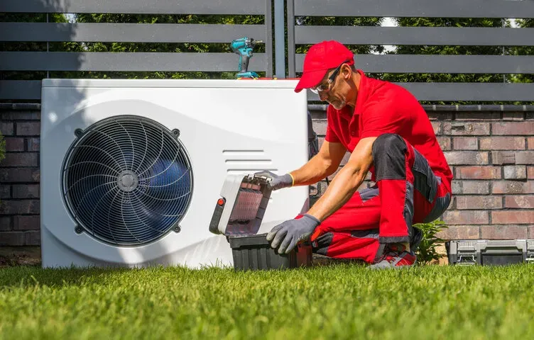 HVAC technician in red uniform servicing air conditioning unit.