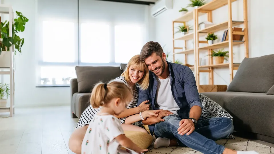 Famiglia di tre persone seduta insieme sul pavimento che legge un libro.