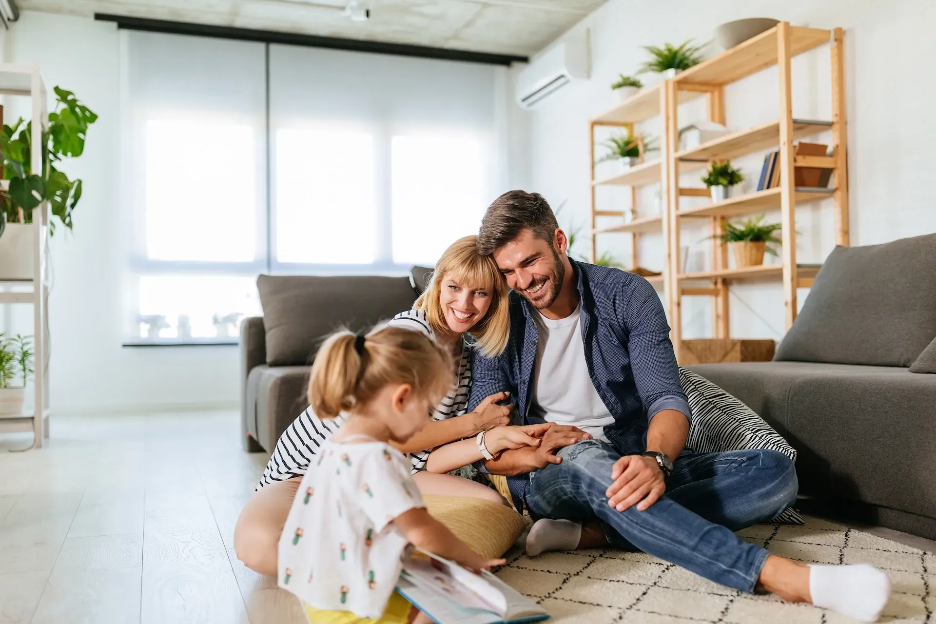 Famiglia di tre persone seduta insieme sul pavimento che legge un libro.