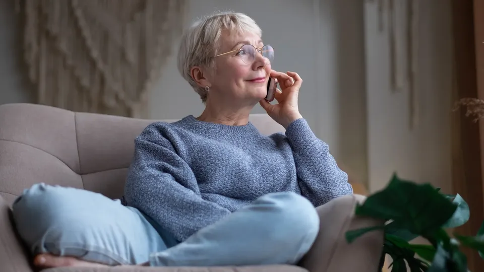 Ældre kvinde på sofa taler i telefon.