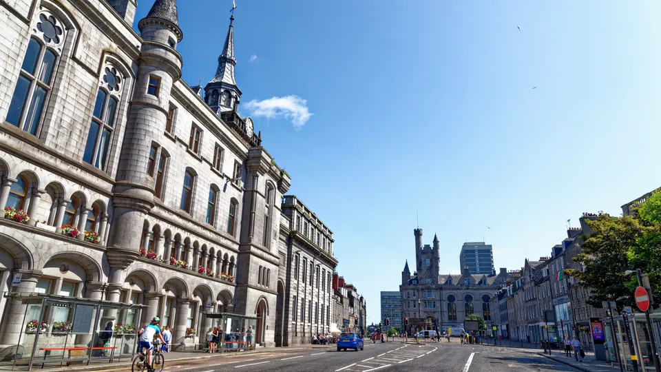Cyclist riding on a city street lined with historic stone buildings under clear blue sky.
