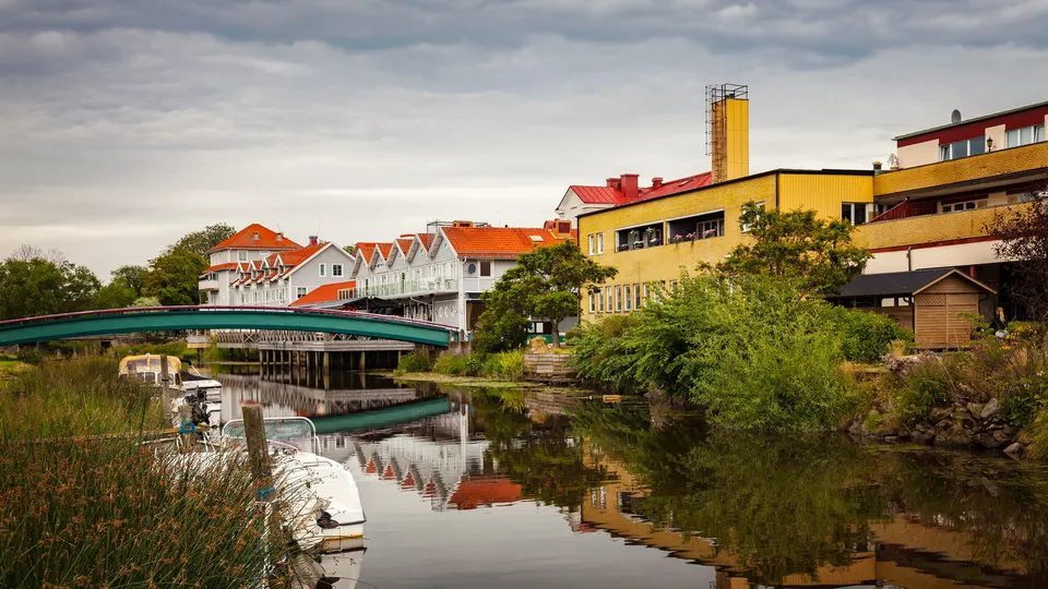Färgglada vattenfrontbyggnader reflekterade i lugnt kanalvatten med grön bro.