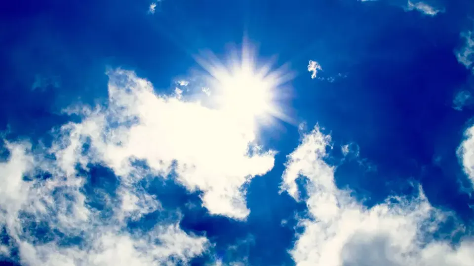 Et klart soludbrud på en dybblå himmel med tynde, hvide skyer formidler en følelse af ro og sindsro. Sollyset skaber en strålende glød.