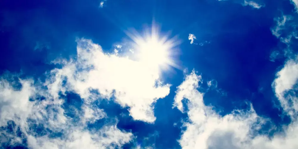 Et klart soludbrud på en dybblå himmel med tynde, hvide skyer formidler en følelse af ro og sindsro. Sollyset skaber en strålende glød.