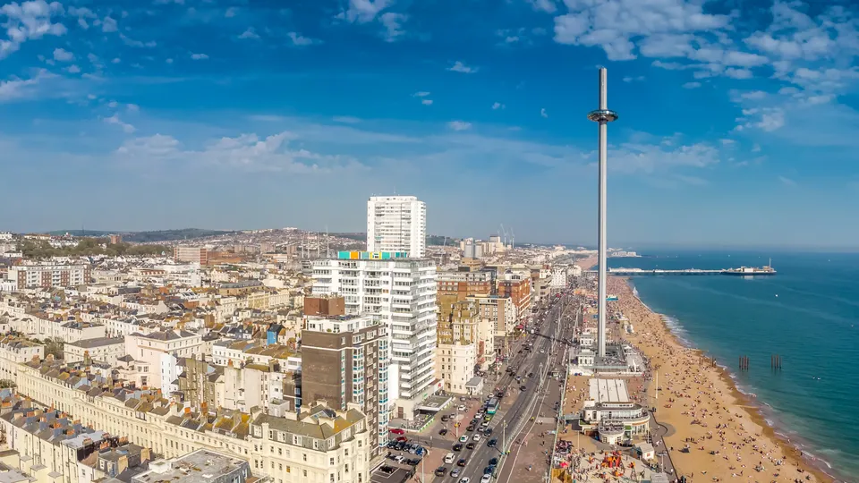 Aerial view of Brighton beachfront with sandy beach, seafront promenade, and residential buildings under blue sky.
