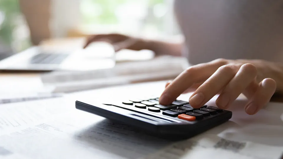 Mano di una persona che usa una calcolatrice su documenti finanziari.