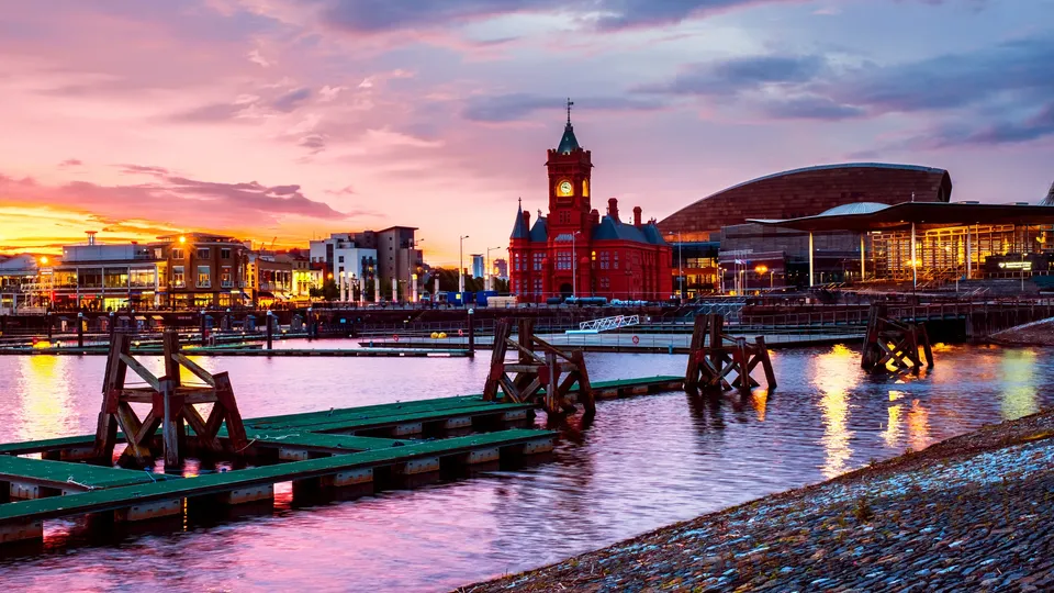 Waterfront at sunset with wooden dock structures and red clock tower building across the water.