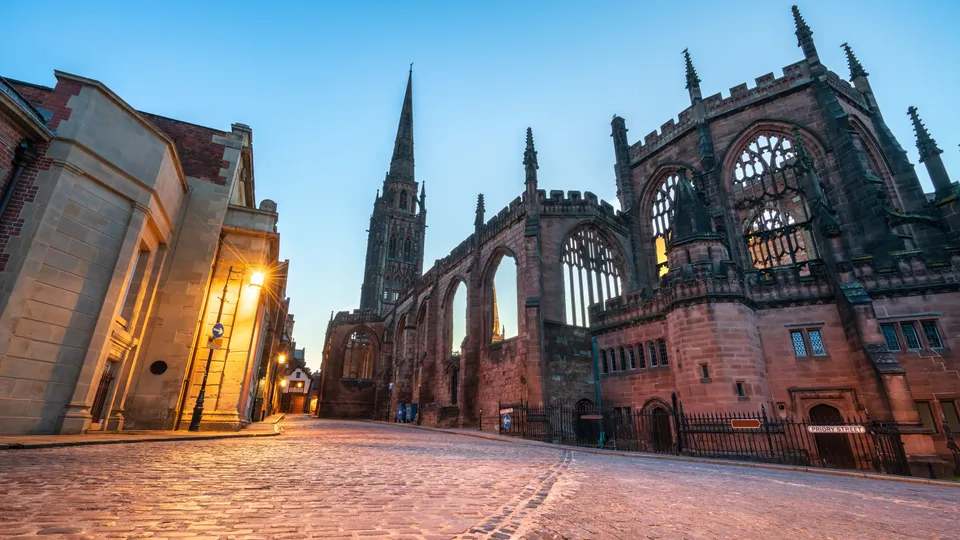 Historic stone cathedral ruins with Gothic architecture and illuminated buildings at dusk.