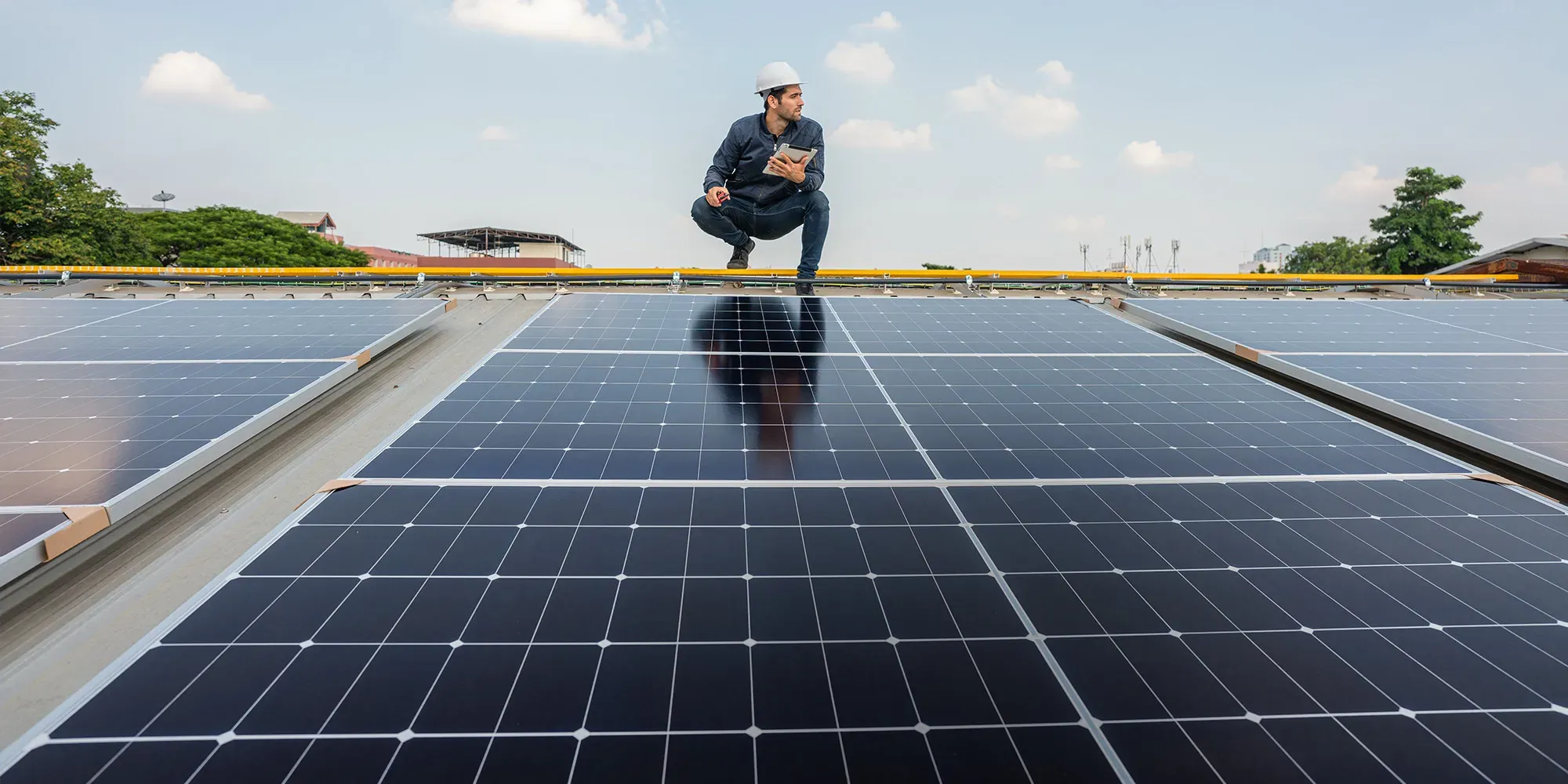 Mitarbeiter eines Photovoltaik-Unternehmens prüft mit Tablet die Solarmodule auf einem Dach.