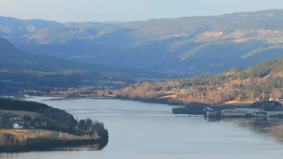 Panoramautsikt over en elvedal omgitt av skogkledde åser og fjerne fjell.