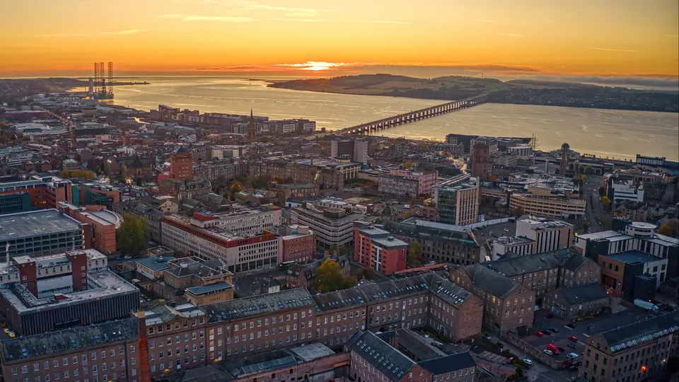 Sunset over Dundee cityscape with bridge spanning water.