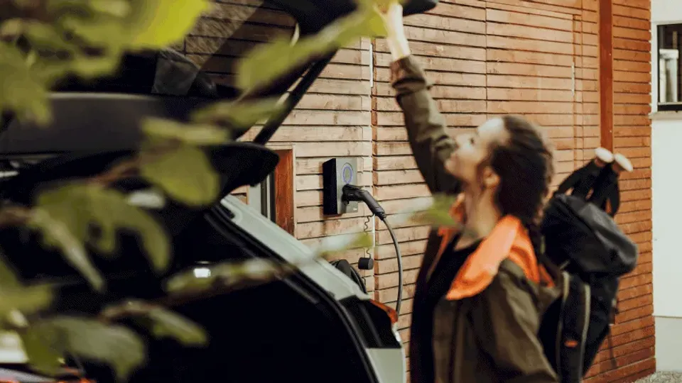 Person installing a home EV charger on a wooden wall beside a parked electric car