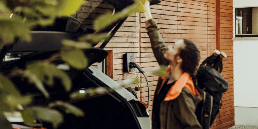Person installing a home EV charger on a wooden wall beside a parked electric car