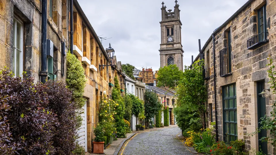 Cobblestone street lined with stone buildings and ivy, church tower visible ahead.