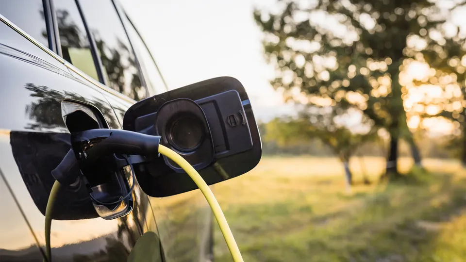 Elektrisk køretøj oplades med gult kabel i naturomgivelser.
