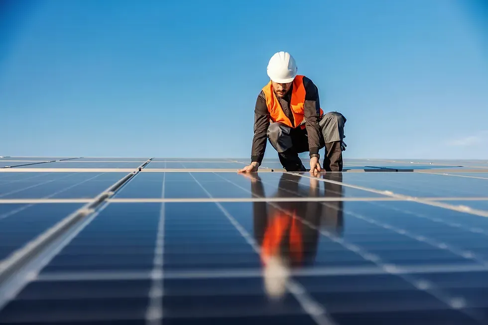 Un tecnico con caschetto bianco controlla i pannelli solari sul tetto, sotto un cielo azzurro.