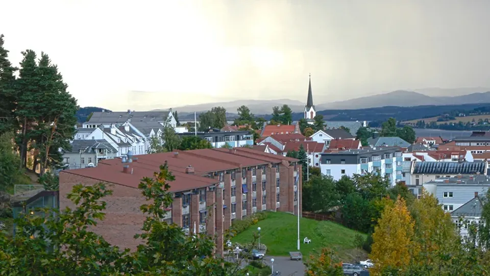 Utsikt over en by med et kirkespir og åser i bakgrunnen.