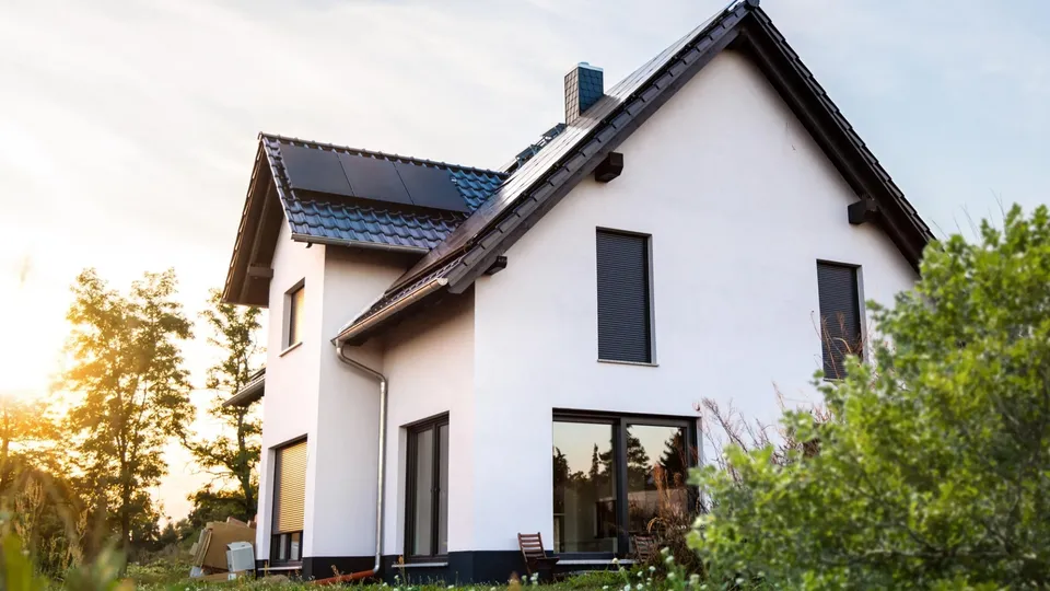 Modernes weisses Haus mit Solarpanelen auf dem Dach und grossen Fenstern.