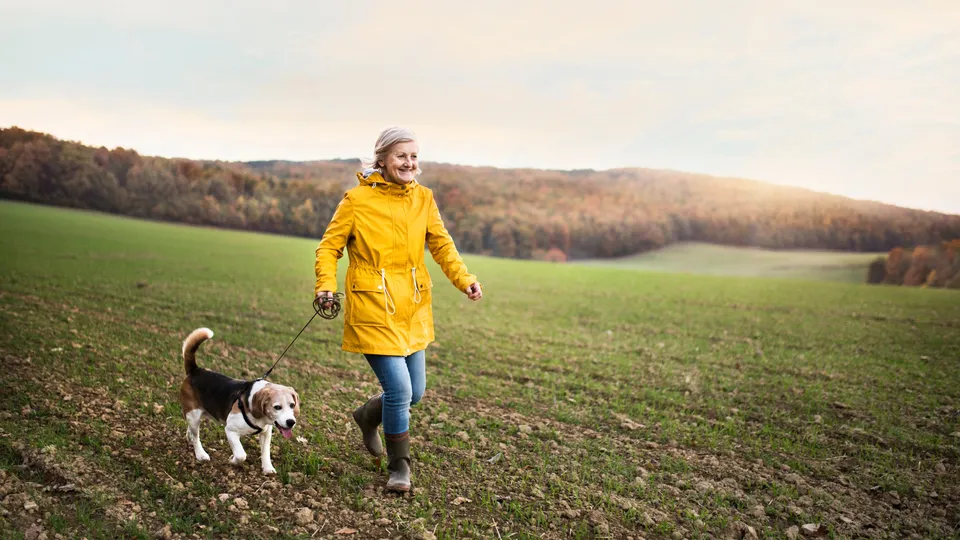 Ældre kvinde løber med hund på åben mark.