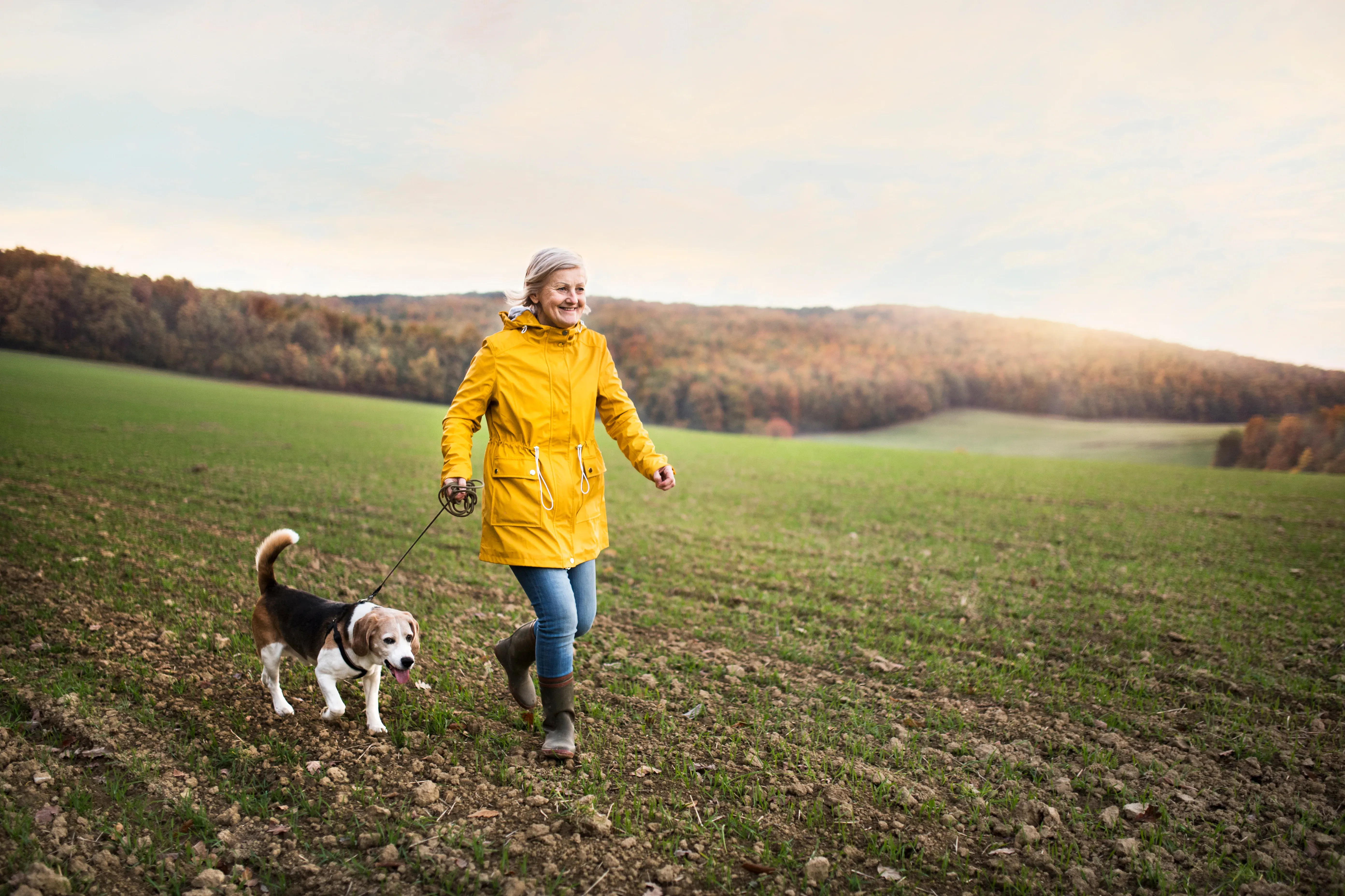 Ældre kvinde løber med hund på åben mark.