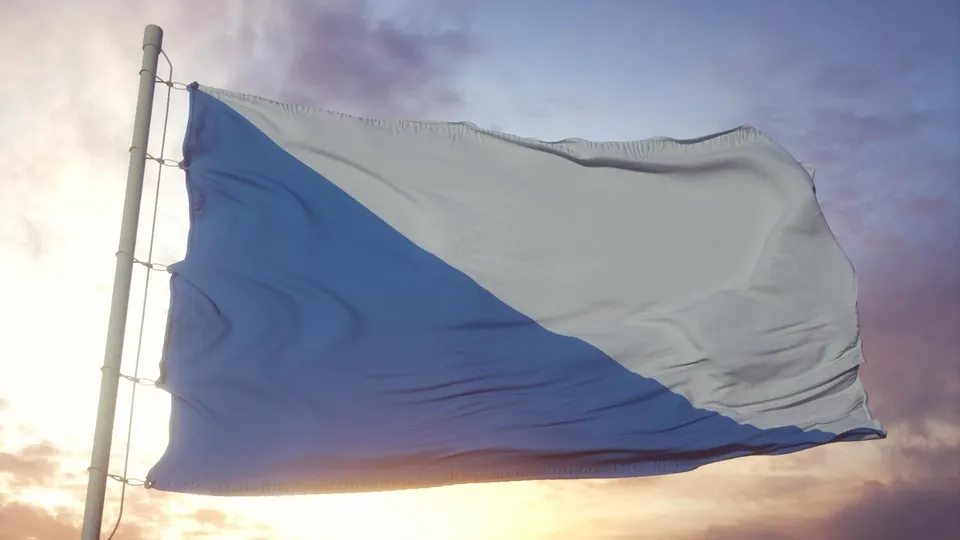 Blau-weisse Flagge weht an Fahnenmast bei Sonnenuntergang.