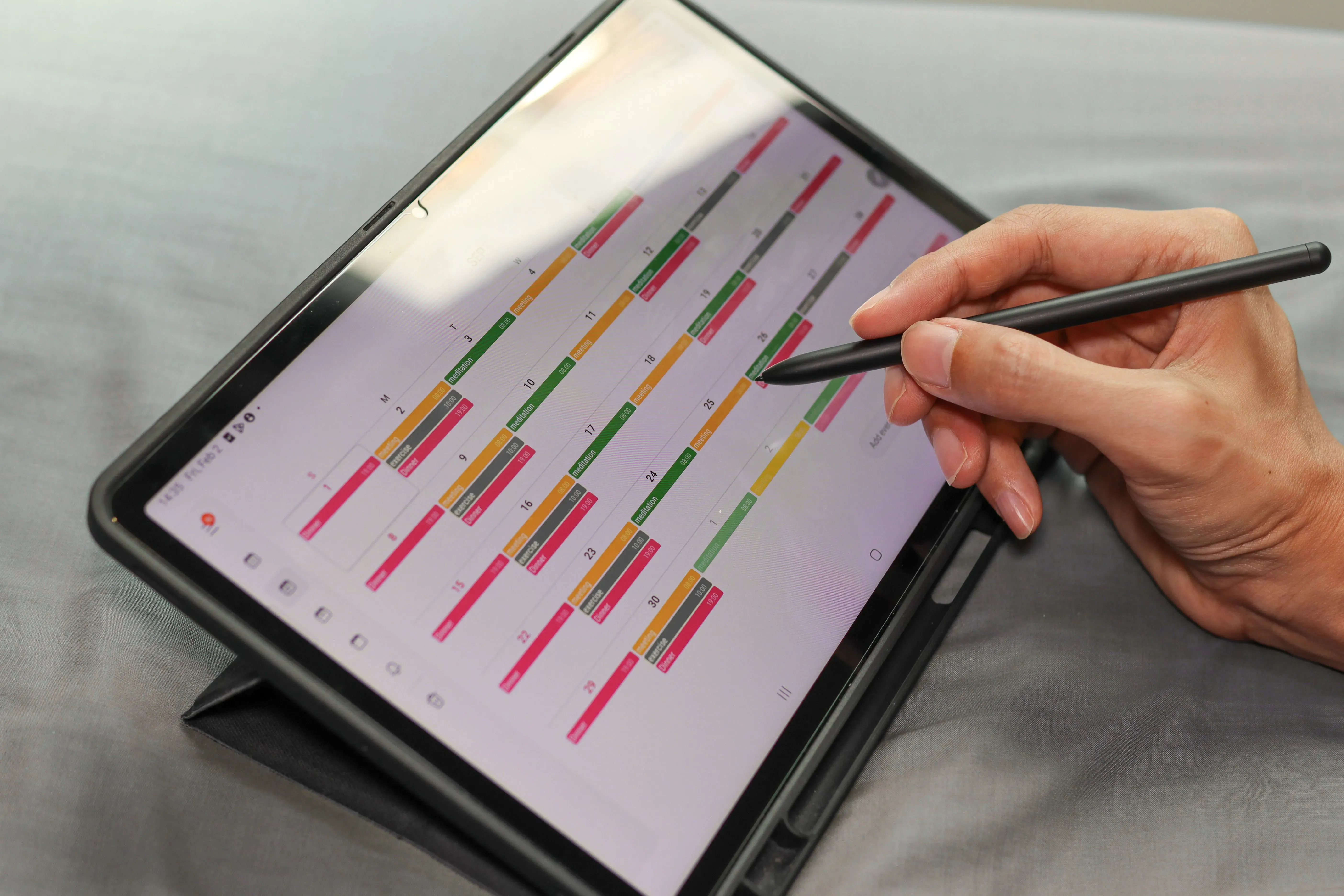 Hand bedient mit einem Stift einen digitalen Termin- und Projektplan auf einem Tablet.
