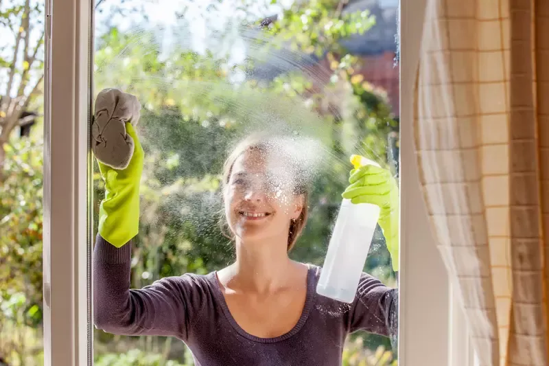 Kvinna rengör fönster med sprayflaska och trasa.