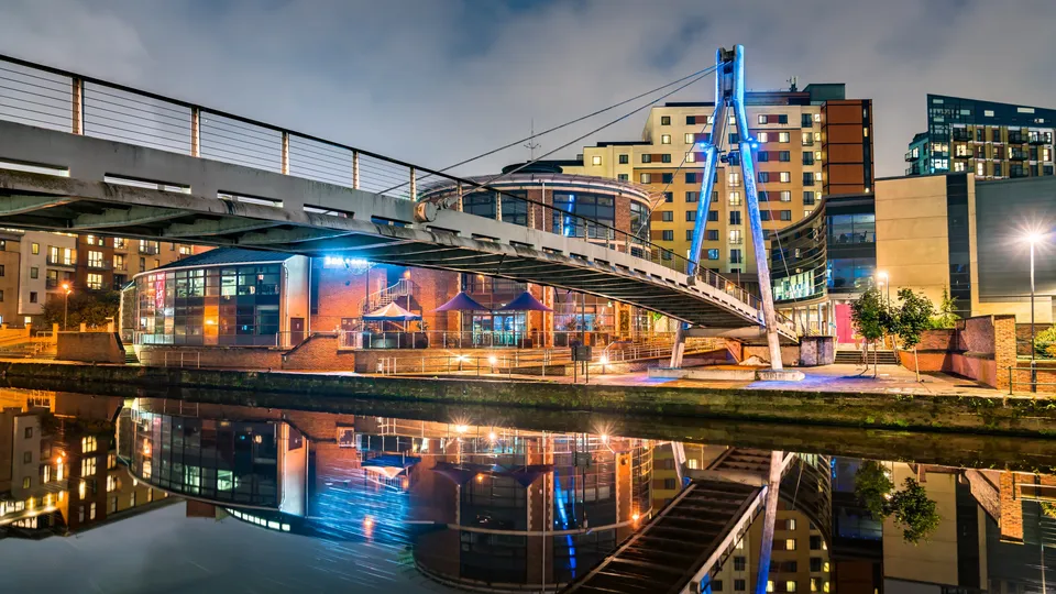 Illuminated riverside building with blue bridge reflected in still water at dusk.