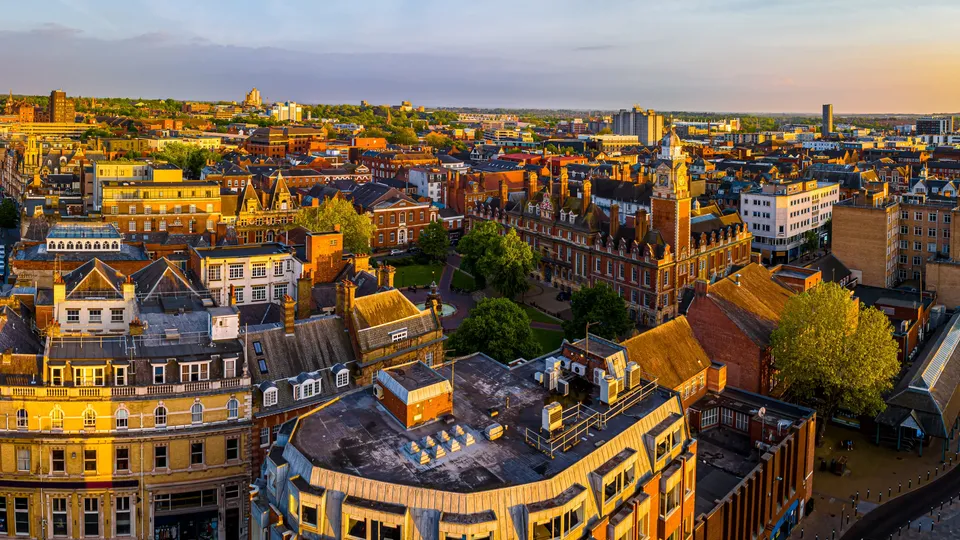 Aerial view of Leicester city center with golden-hour sunlight illuminating historic brick buildings and streets.