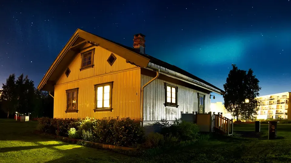 Gult trehus opplyst om natten med stjernehimmel over.