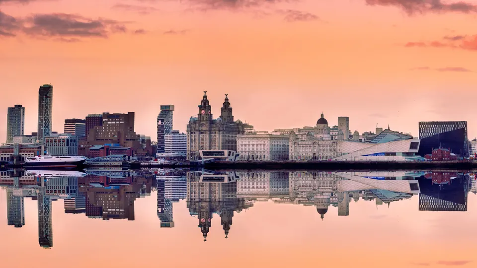 Liverpool waterfront skyline reflected in still water at sunset.