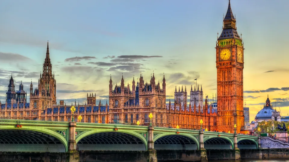 Big Ben and Houses of Parliament illuminated at sunset with Westminster Bridge spanning the River Thames.