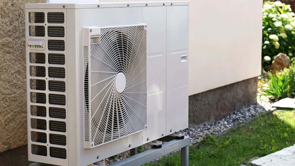 Außenwärmepumpenanlage mit Ventilator auf Betonsockel neben Haus.