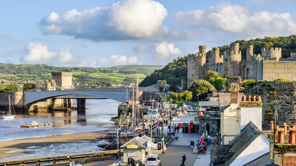 Medieval castle overlooking harbor with boats and bridge.