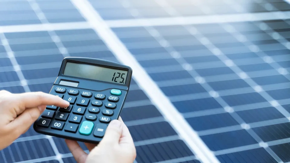 Person berechnet mit einem Taschenrechner vor einem Solarmodul die Kosten einer Photovoltaikanlage.