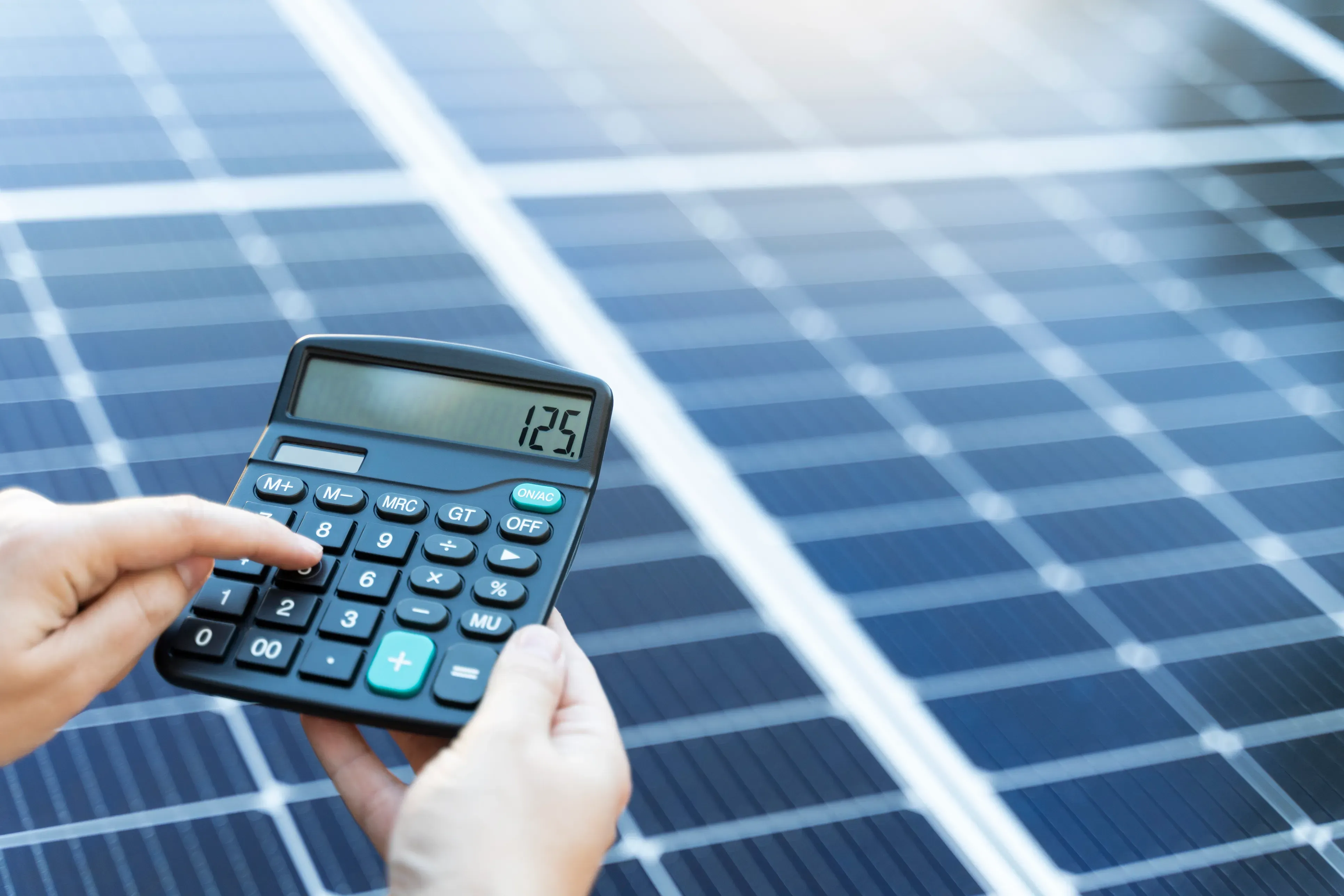 Person berechnet mit einem Taschenrechner vor einem Solarmodul die Kosten einer Photovoltaikanlage.