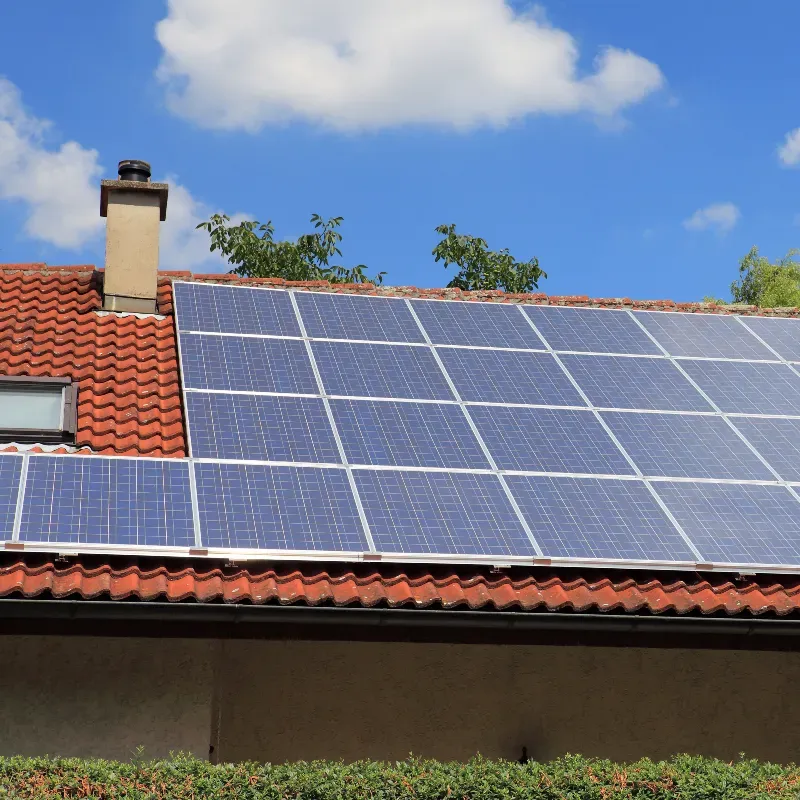 Solar panels installed on a residential roof with red tiles and chimney.