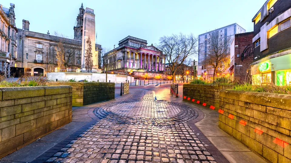 Illuminated city square with paved pathway leading toward historic buildings at dusk.