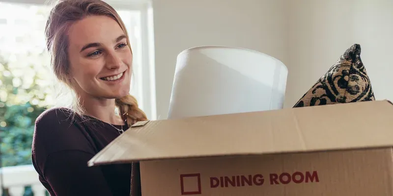 Kvinde smiler mens hun åbner flyttekasse mærket med spisestue.