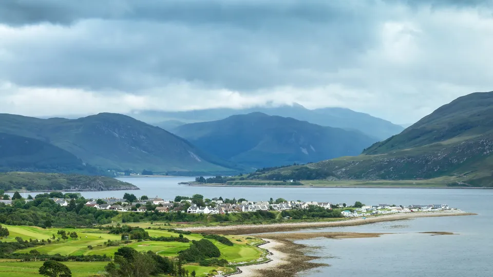 Coastal village nestled between green hills and mountains along a Scottish loch.