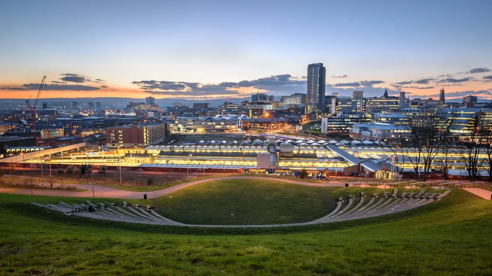 Amphitheater seating overlooking illuminated industrial buildings and city skyline at dusk.
