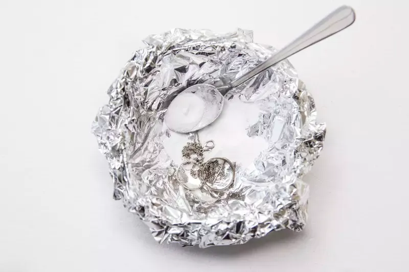 Sked vilande på skrynklig aluminiumfolie med bakpulver och mätskedar.