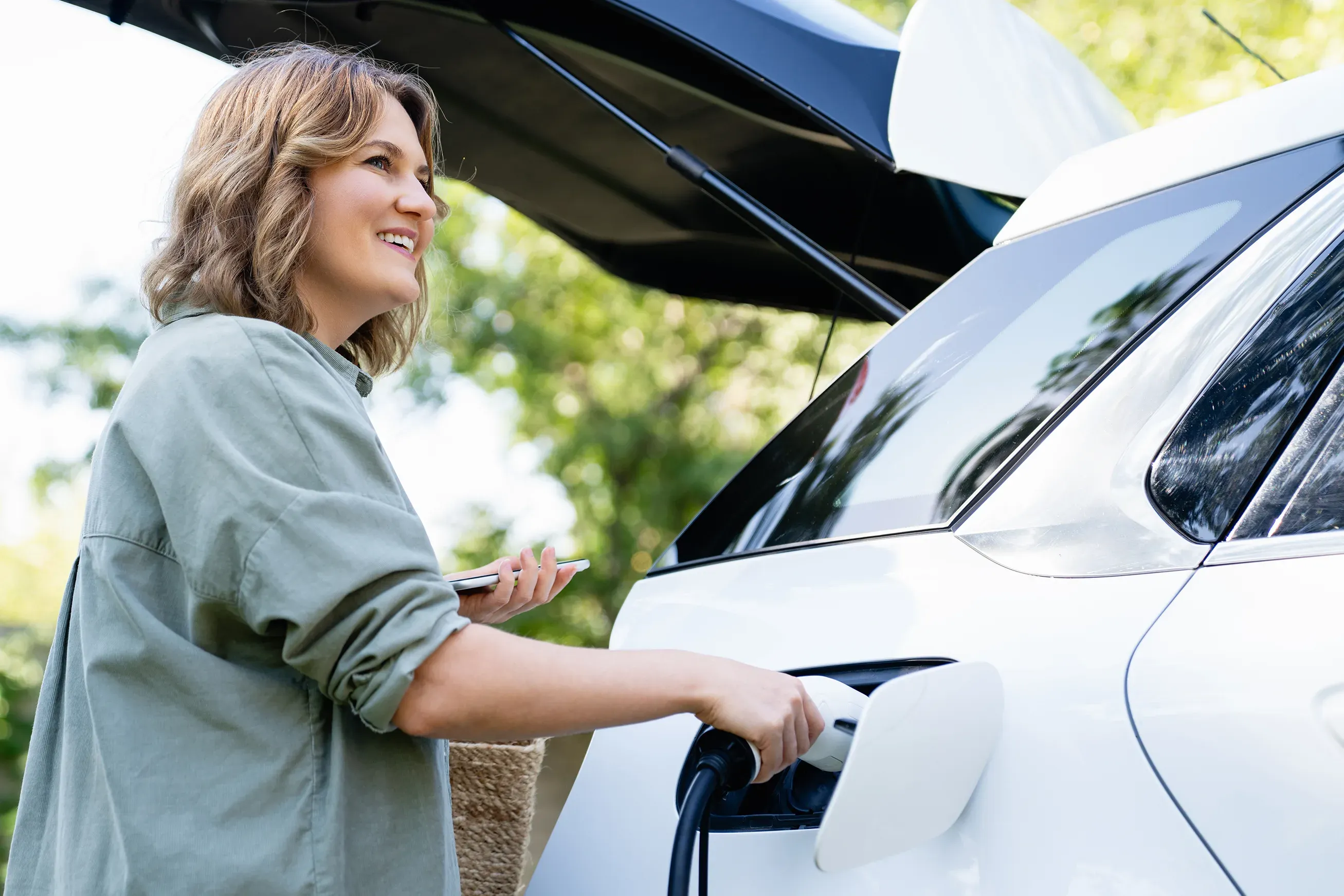 Donna carica l'auto elettrica mentre tiene in mano il cellulare