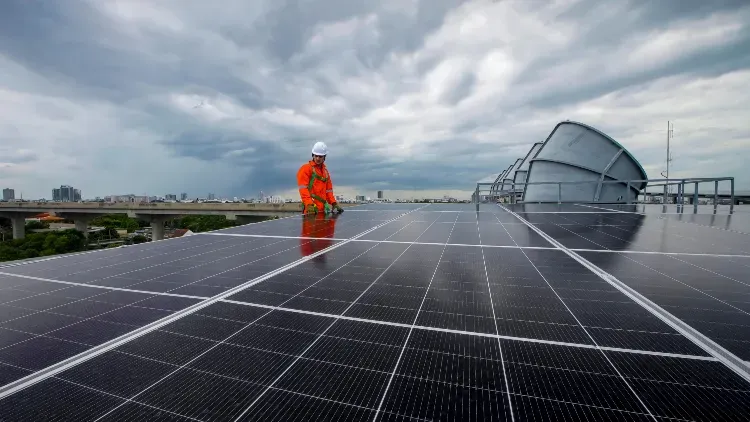 Worker in orange safety gear inspecting rooftop solar panels.