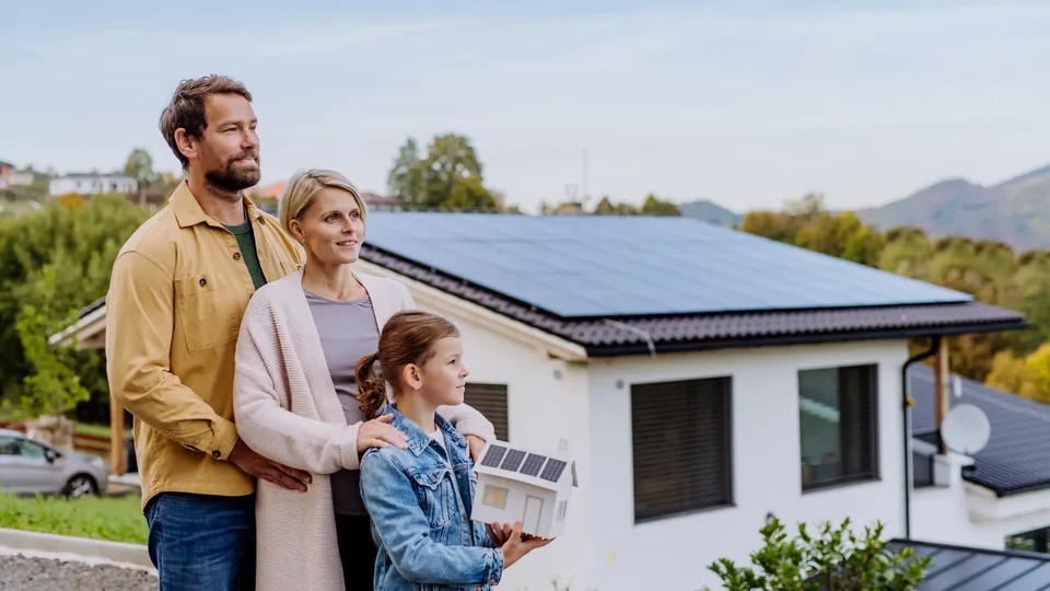 Family standing outside house with solar panels on roof.