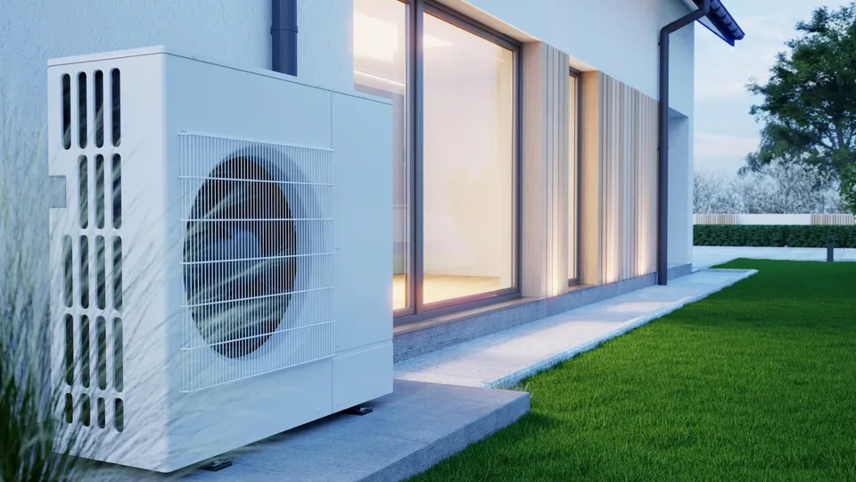 Weiße Wärmepumpenanlage außen an modernem Haus mit großen Fenstern installiert.