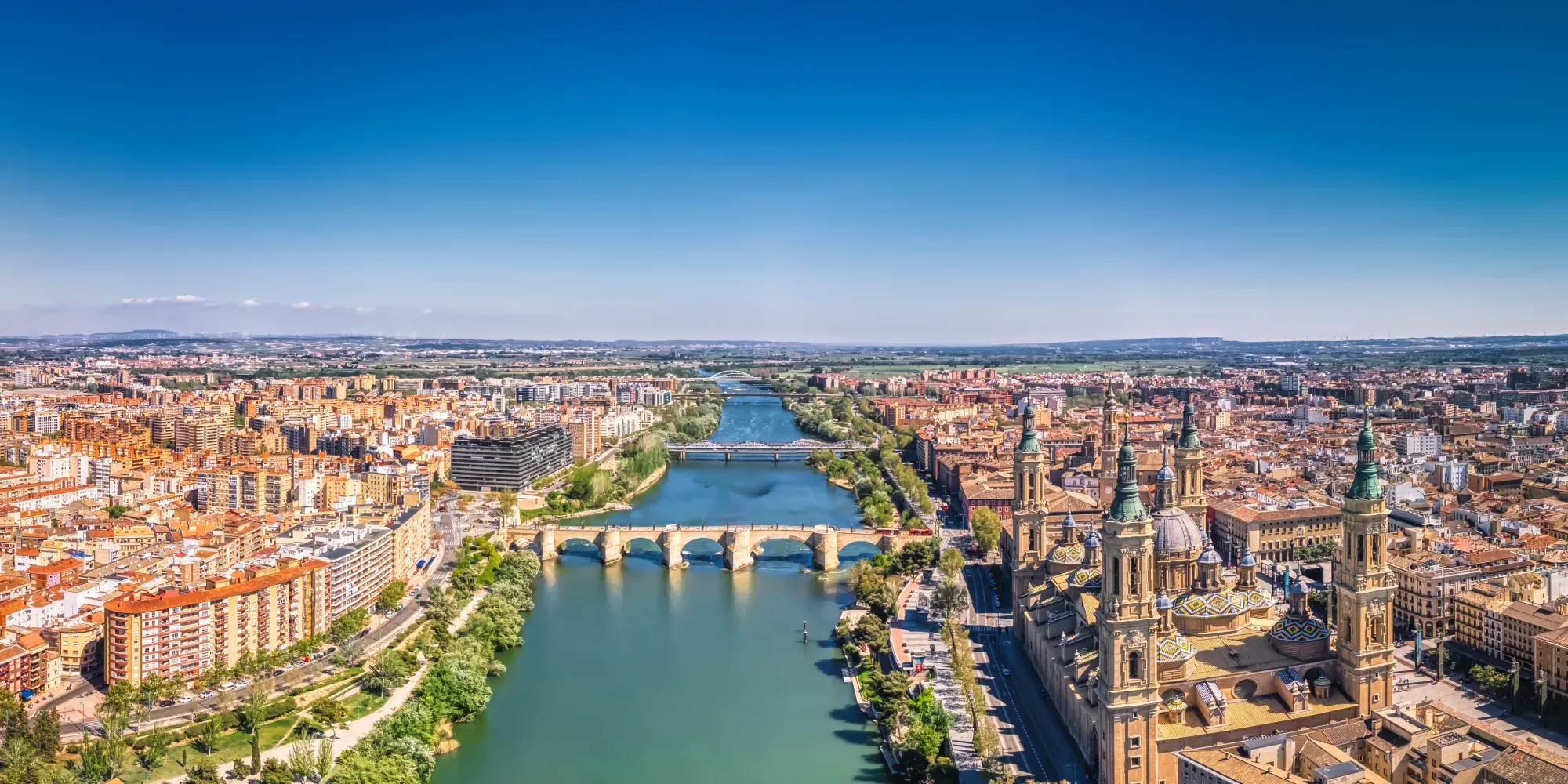 Vista aérea del paisaje urbano de Zaragoza con río y puente de piedra.