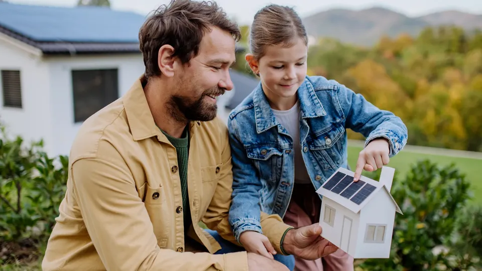Father and daughter examining a miniature house model with solar panels.