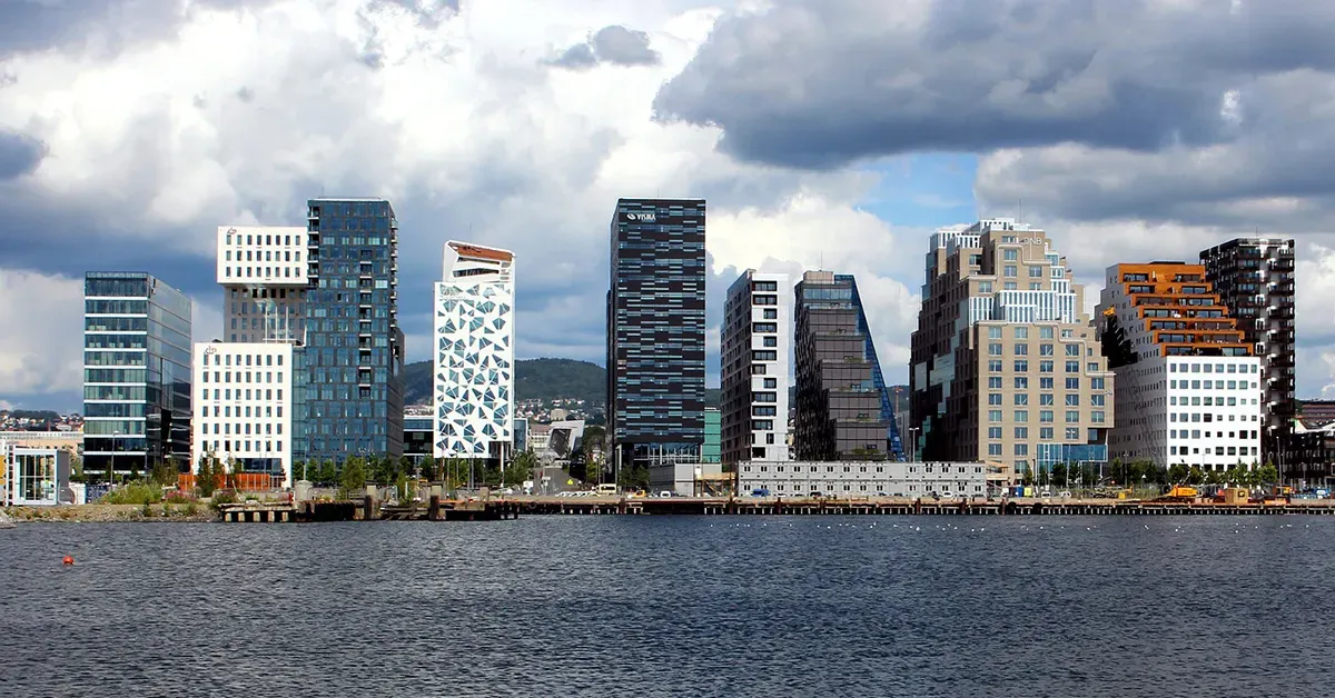 Moderne høyhus langs en vannkant under skyet himmel.