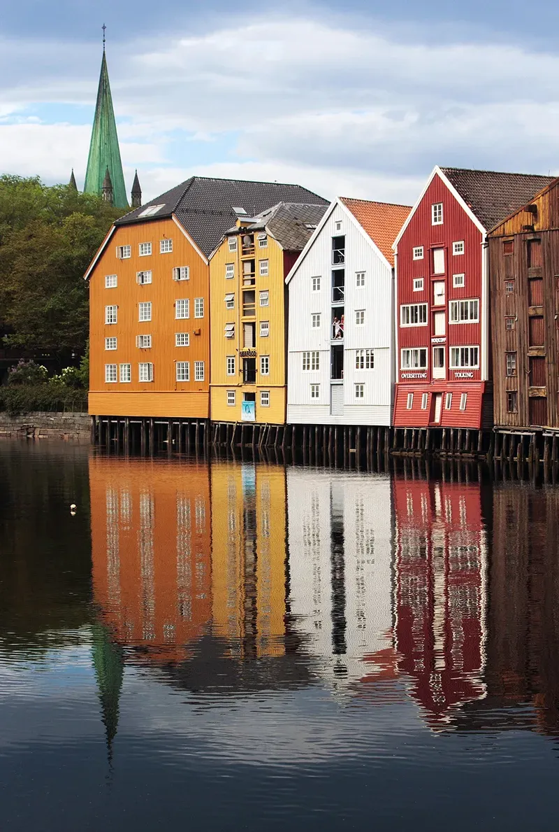 Fargerike trehus på påler reflektert i elvevann.